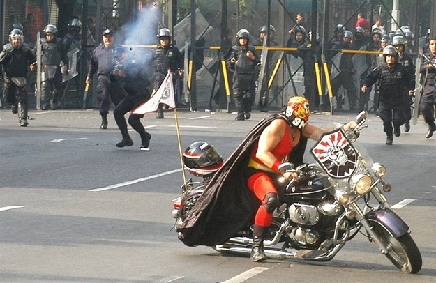 Whoever this luchador riding a motorcycle while riot police fire tear gas at him is
